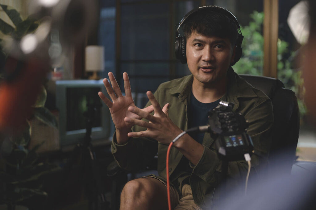 Male podcaster gesturing while recording a remote interview in a home studio setup with professional headphones and microphone.