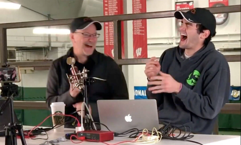 Two male podcast hosts laughing together while recording an episode in a professional studio setup.