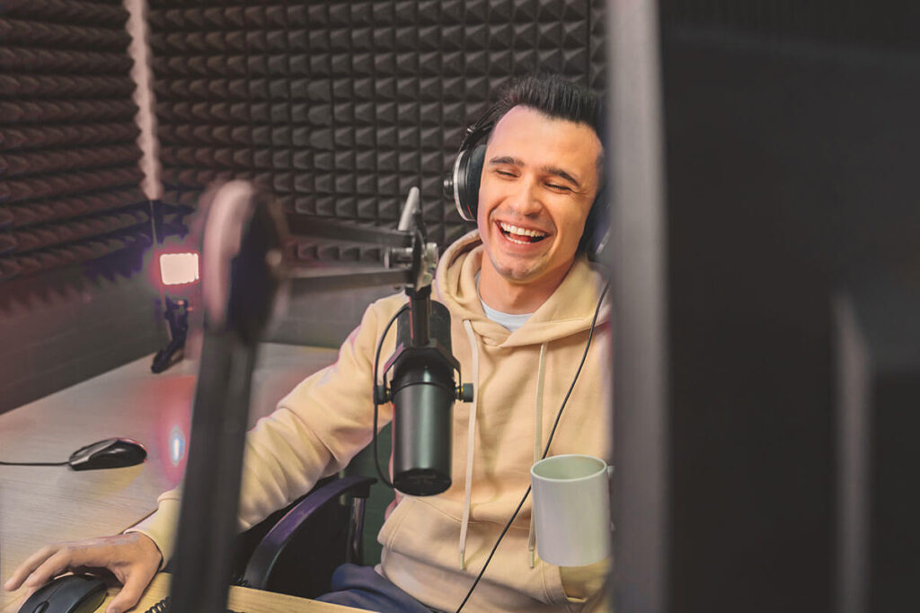 A man recording a sports podcast episode alone in a soundproof booth with a microphone and headphones.